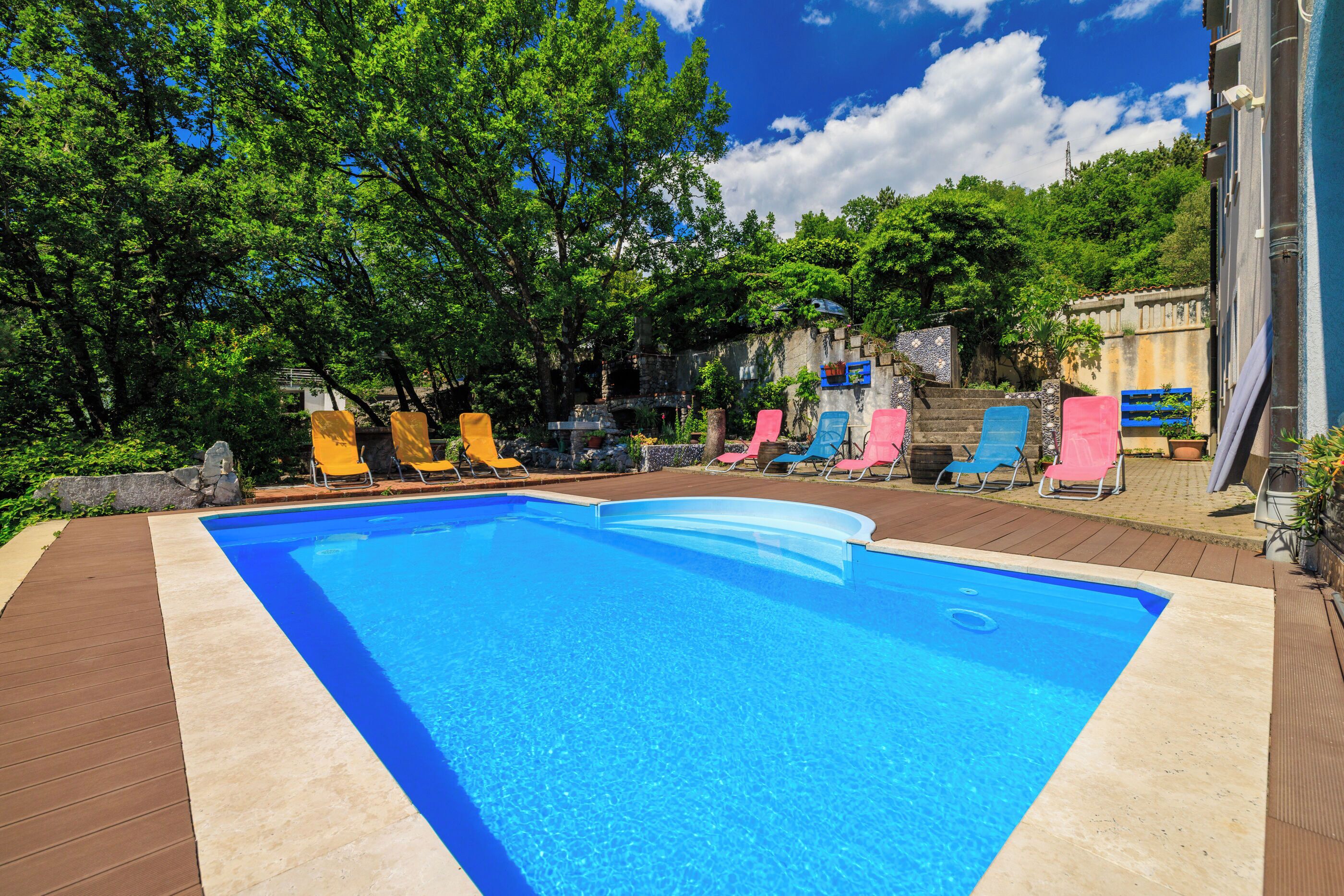 A rectangular swimming pool with clear blue water, surrounded by a wooden deck.