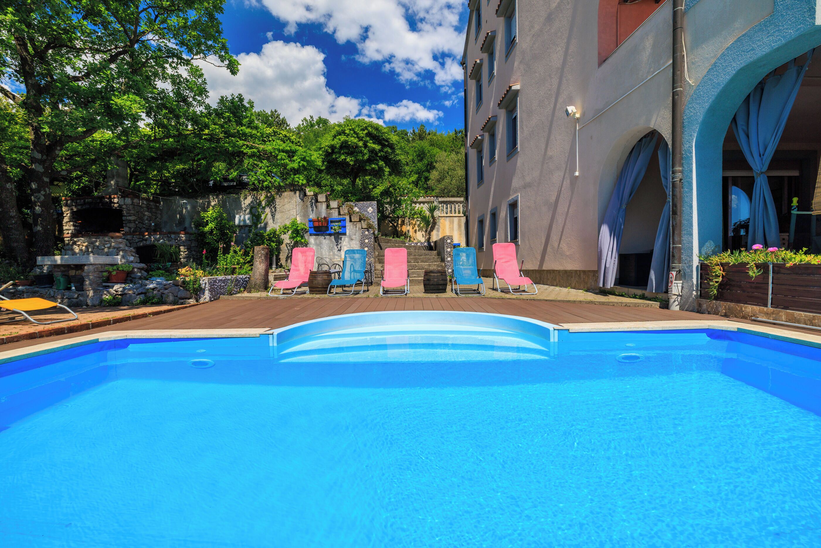 A swimming pool with lounge chairs, a stone structure, and a building with arches.