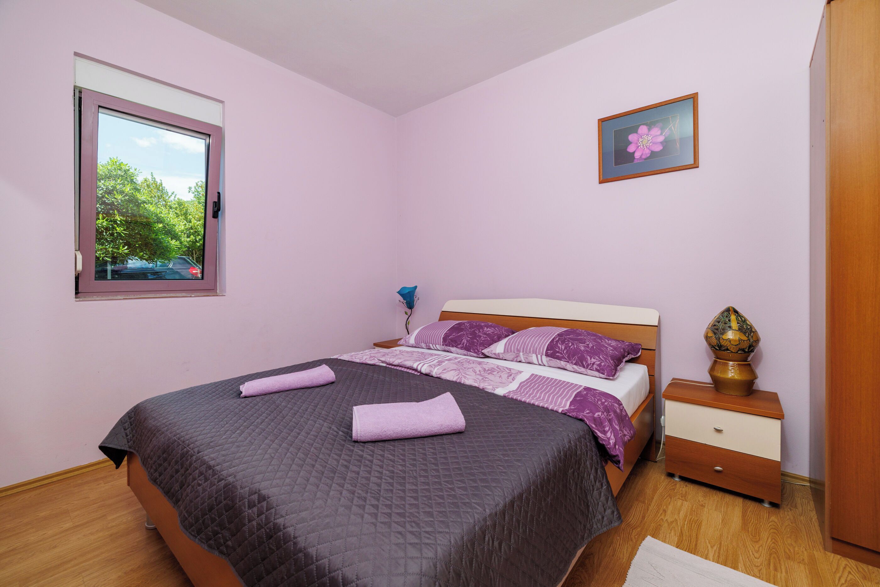 Un dormitorio con cama, mesita de noche, cómoda, ventana con vistas y un cuadro en la pared.