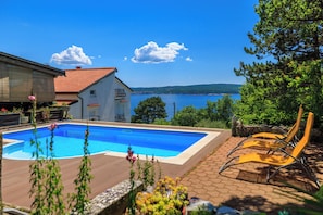 A swimming pool with a view of the sea, a house with a red roof, and a stone wall.