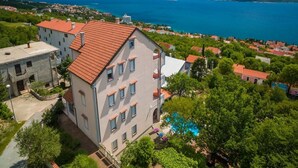 A multi-story building with a red-tiled roof, surrounded by greenery and a swimming pool. - Apartments Djusi (Dramalj)