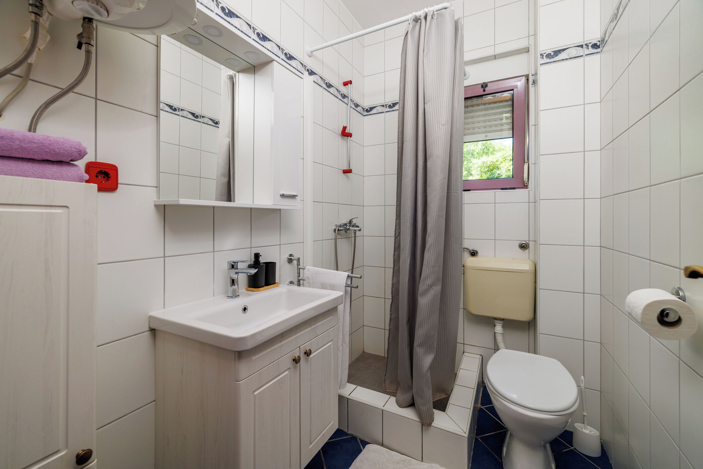 A bathroom with a white sink, mirror, toilet, and shower curtain.