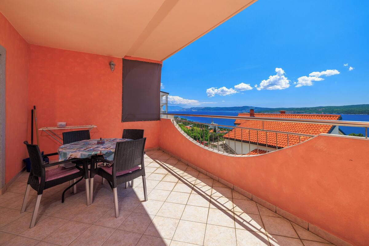 Un balcon avec une table et des chaises, une vue sur la mer et un sol carrelé.