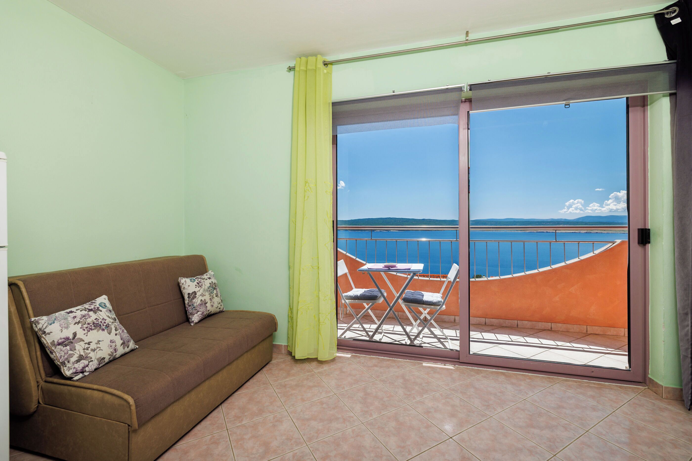 A balcony with a view of the sea, a sofa with floral cushions, and a table with chairs.