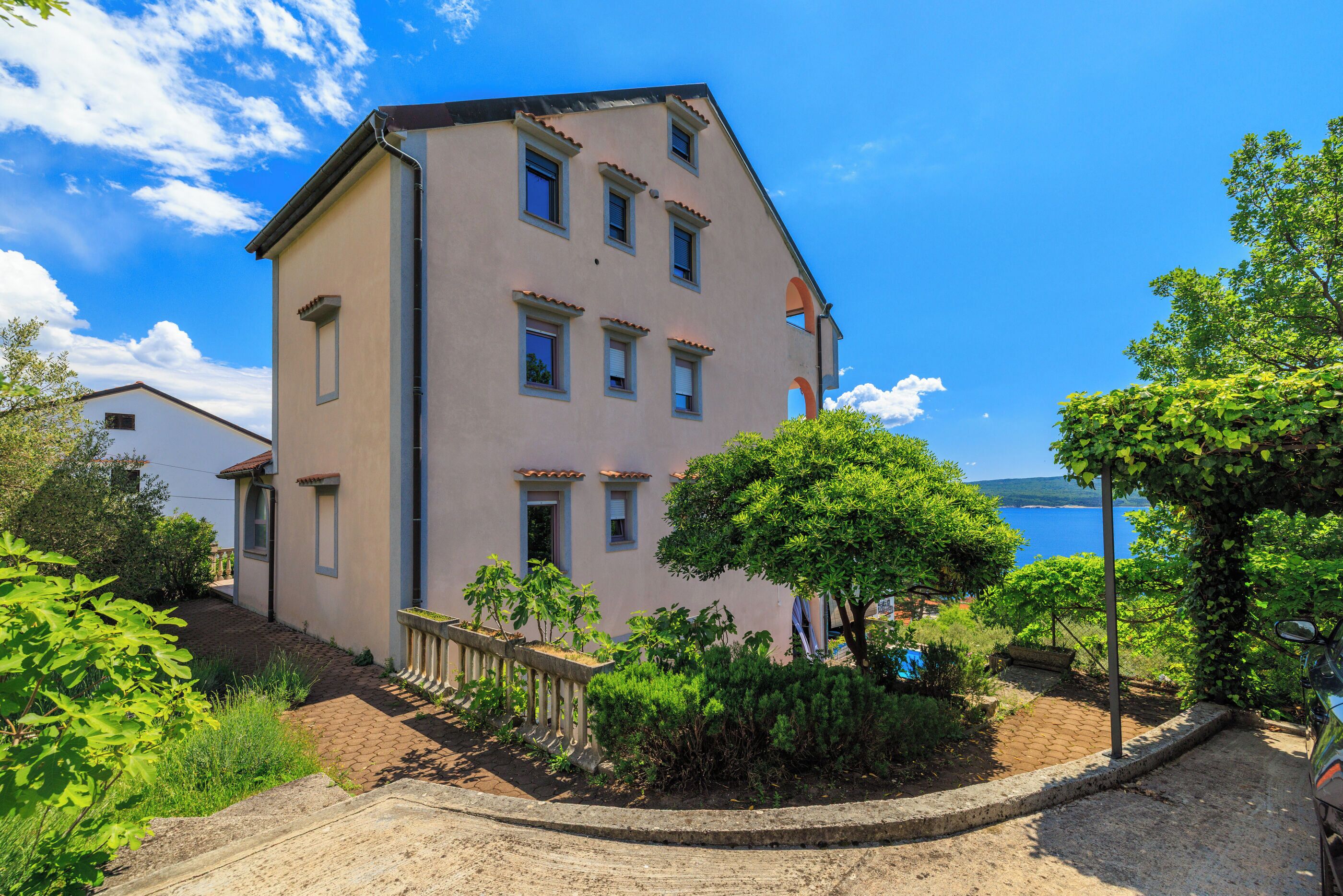 A multi-story building with a balcony, a paved driveway, and a view of the sea.