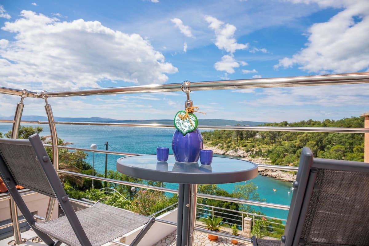 A balcony with a table, chairs, and a view of the sea.