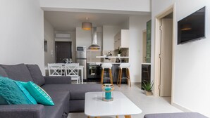 Un salon moderne avec un canapé gris, une table basse blanche et une cuisine en arrière-plan.