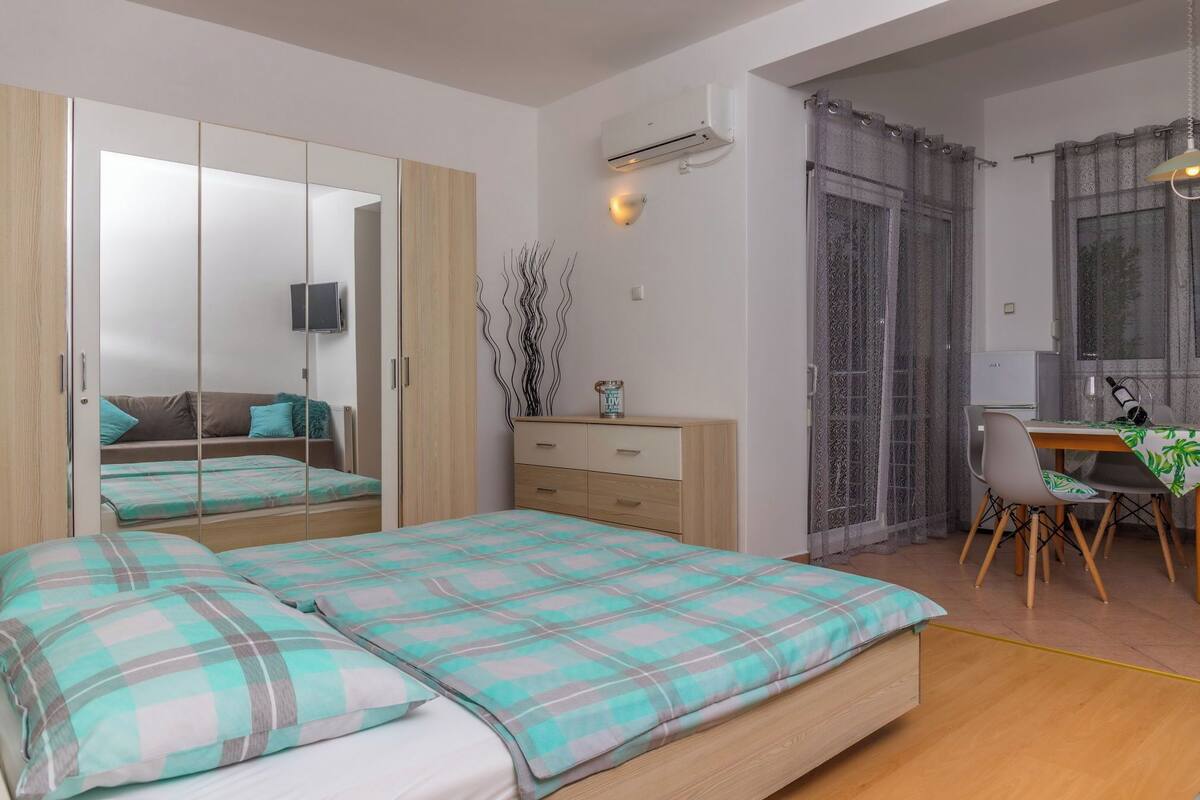 A bedroom with a bed, a wardrobe, a desk, and a dining area.