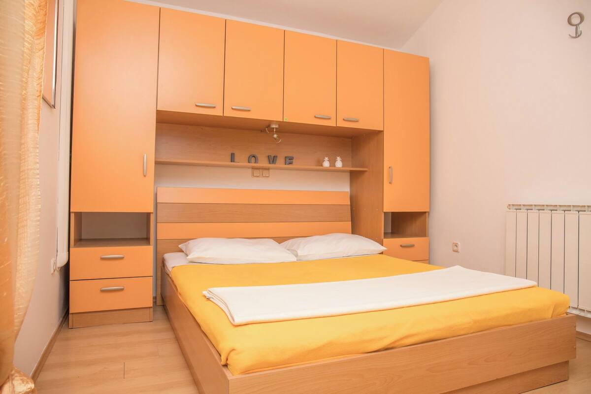 A bedroom with a wooden bed, orange cabinets, and a shelf with the word "LOVE" on it.
