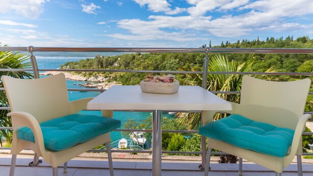 Un balcon avec deux chaises et une table, offrant une vue panoramique sur une plage et une forêt.