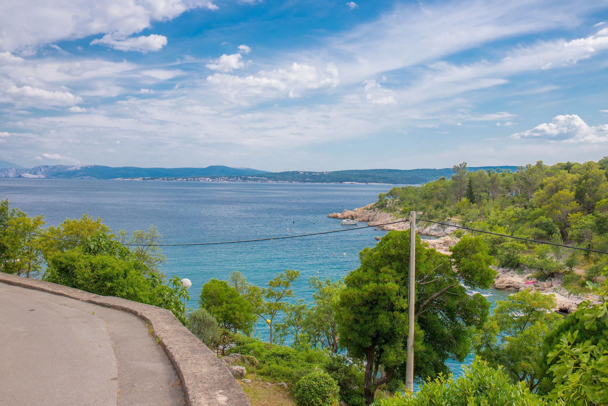 A coastal road with a view of the sea and distant mountains.