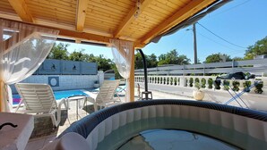 An outdoor pool area with a wooden pergola, lounge chairs, and a hot tub.