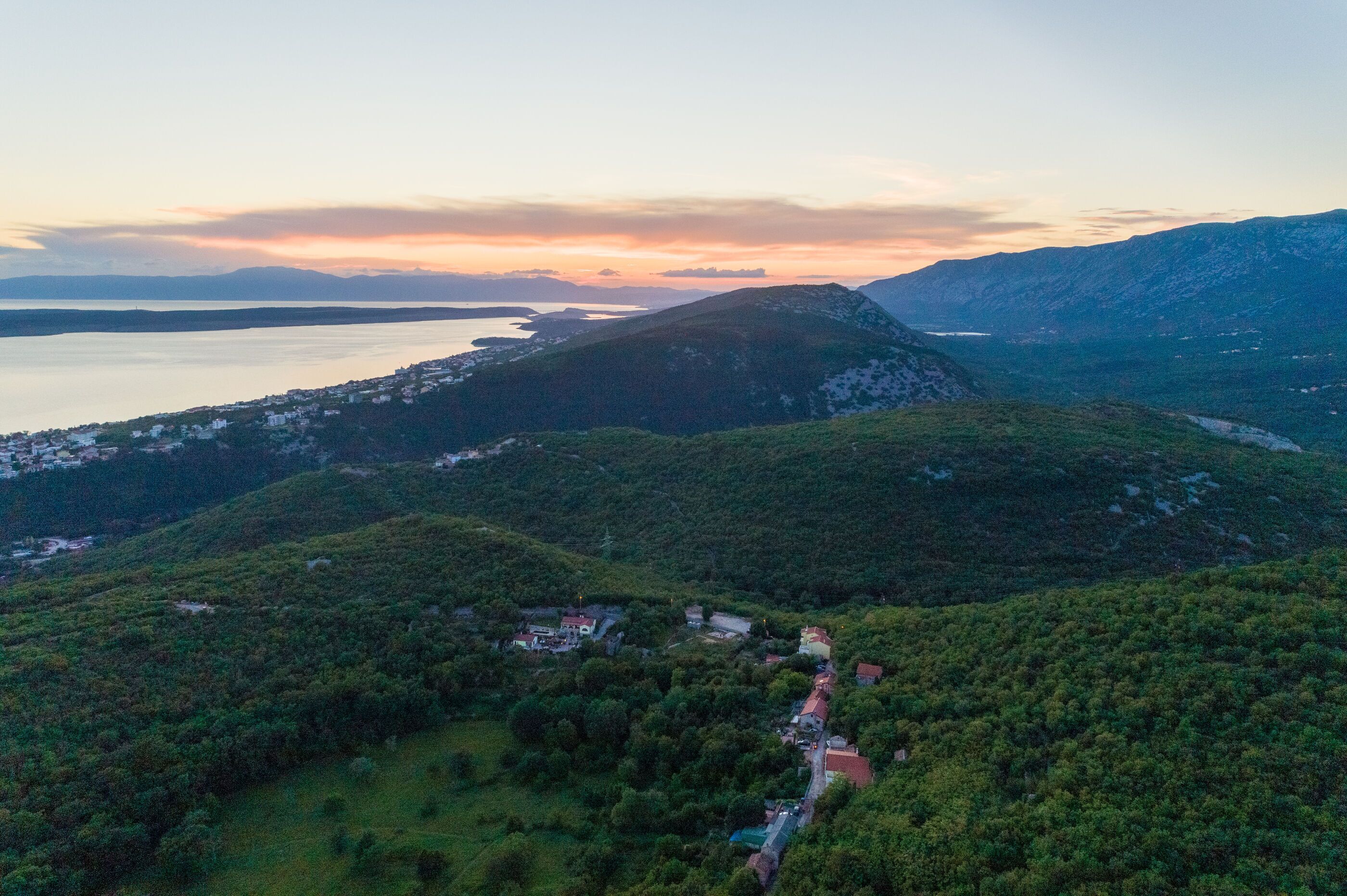 Eine gebirgige Landschaft mit einer kleinen Siedlung und einem Gewässer im Hintergrund.