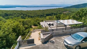 A modern building with a rooftop terrace, surrounded by lush greenery and a lake view. - House Linda 2 (Crikvenica)