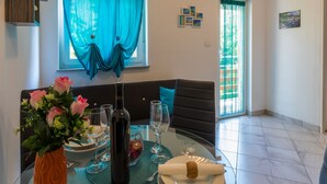 A dining area with a table set for two, a vase of flowers, and a bottle of wine. - Apartment Lena (Crikvenica)