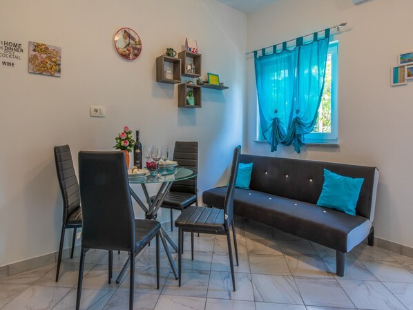 Un coin repas comprenant une table ronde, des chaises, un canapé et une fenêtre avec des rideaux.