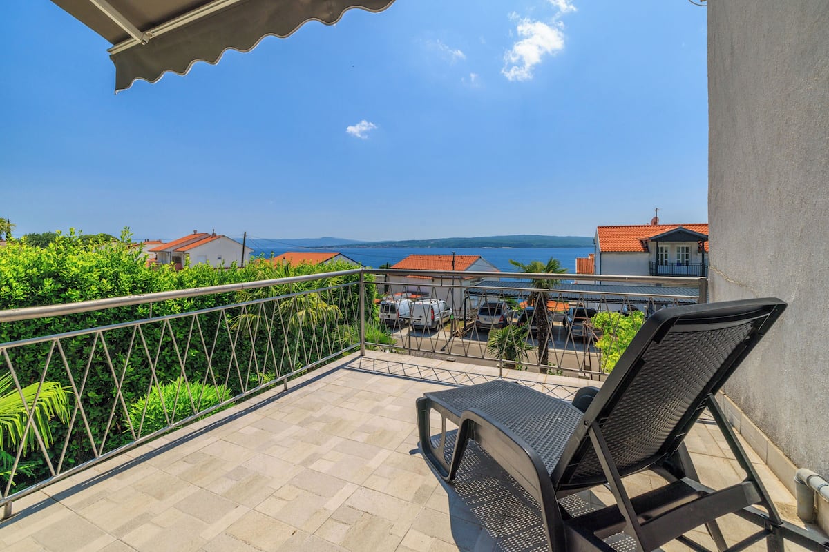 A balcony with a view of the sea, a chair, and a table.
