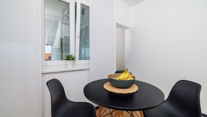 Ein kleiner Essbereich mit einem runden Tisch, zwei schwarzen Stühlen, einer Bananenschale und einem Blumentopf am Fenster.