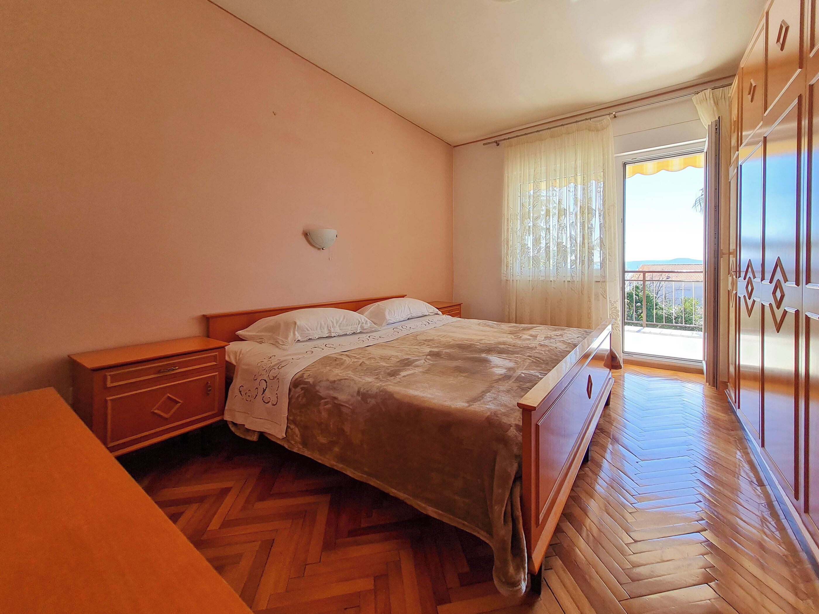 Ein Schlafzimmer mit einem hölzernen Bett, einem Nachttisch, einem Kleiderschrank und einem Fenster mit Vorhängen.