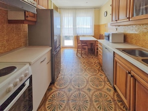 A compact kitchen with a refrigerator, stove, microwave, and sink. There is a dining table with chairs and a window with curtains. - Apartments Antony (Crikvenica)