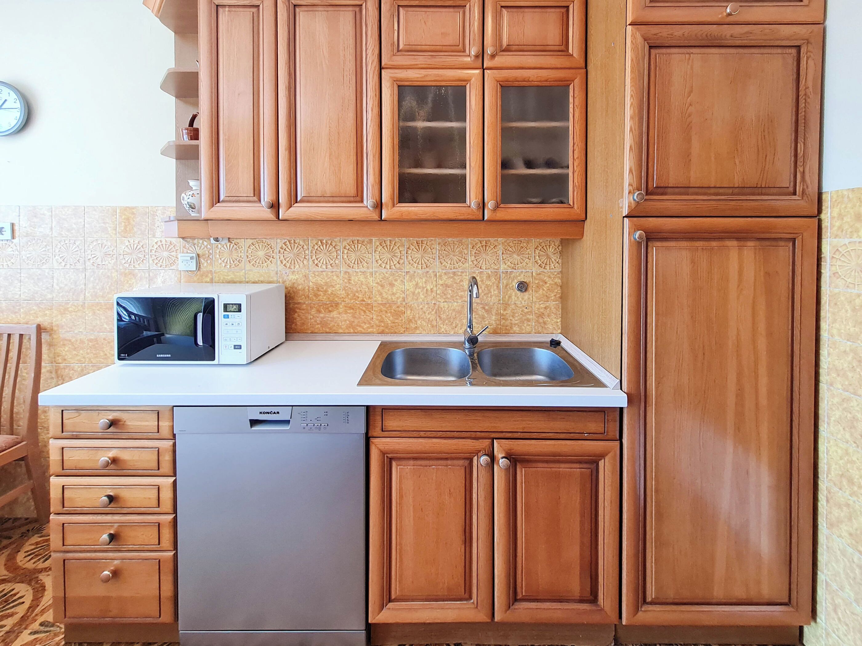 A compact kitchen with wooden cabinets, a microwave, a dishwasher, and a double sink.