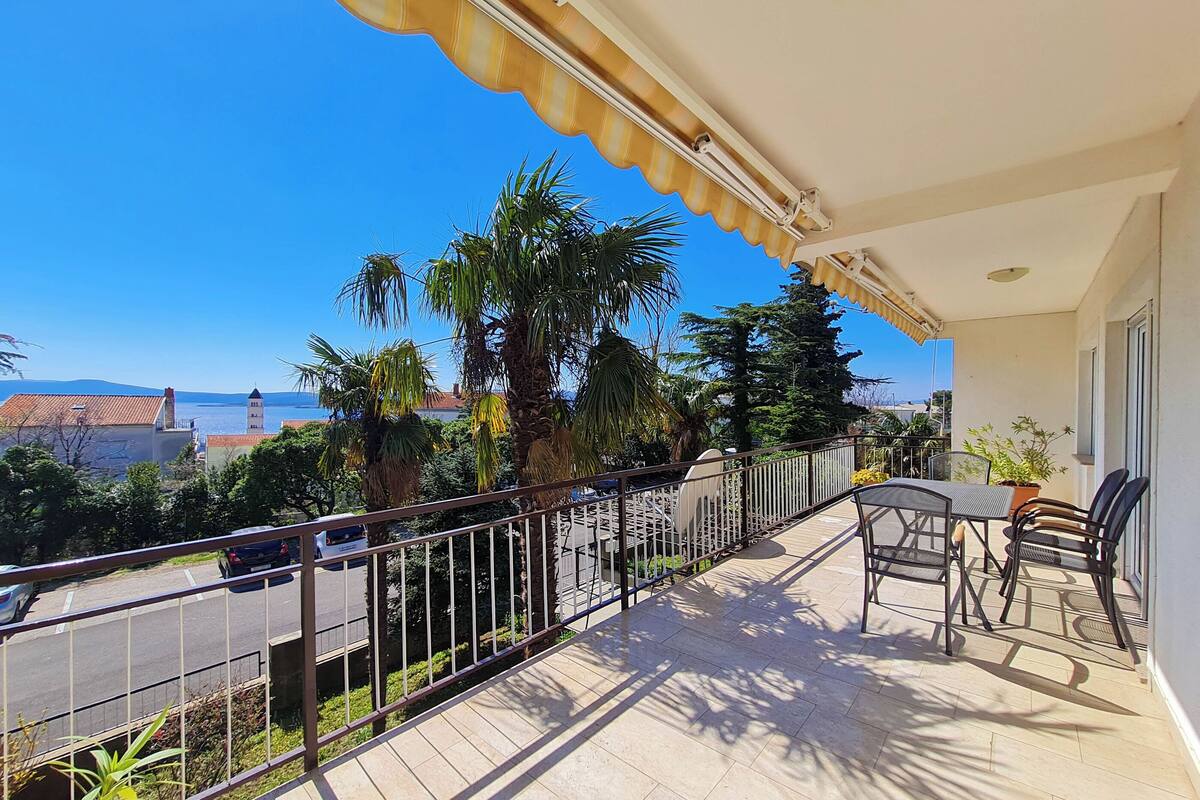 A balcony with a view of the sea, a table with chairs, and a railing.