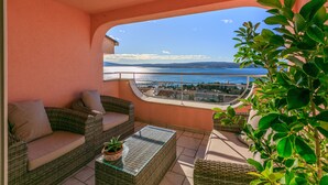 Un balcon agrémenté de meubles en osier, d’une table en verre et offrant une vue sur la mer.