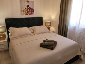 Un letto ben rifatto con una testiera, due lampade ai comodini e un quadro appeso al muro.