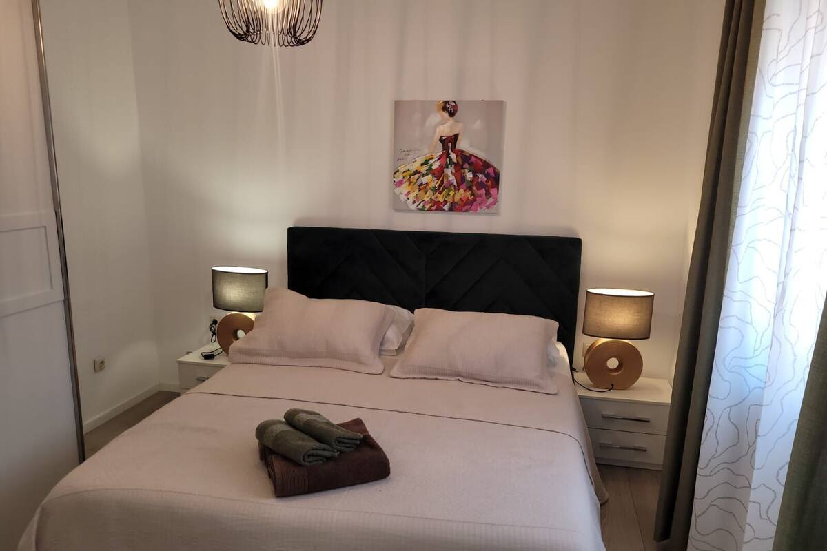 A neatly made bed with pillows, a headboard, bedside lamps, and a towel on the bed.