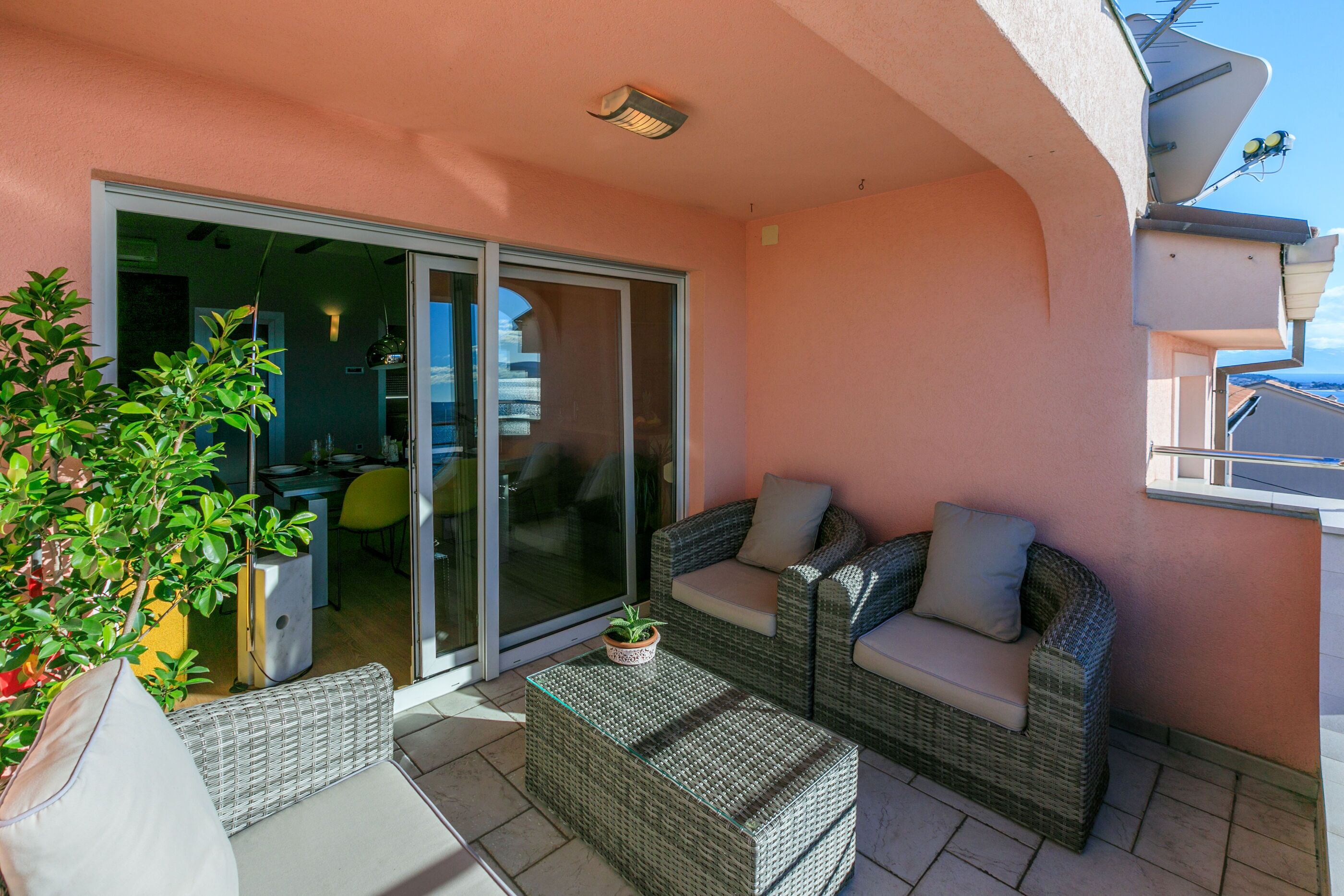 A balcony with wicker furniture, a sliding glass door, and a potted plant.