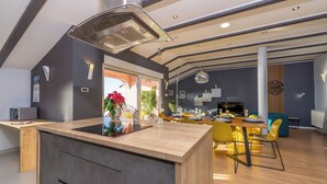 Une cuisine moderne dotée d’un îlot central, d’un coin repas avec des chaises jaunes et d’une grande fenêtre donnant sur un paysage verdoyant.