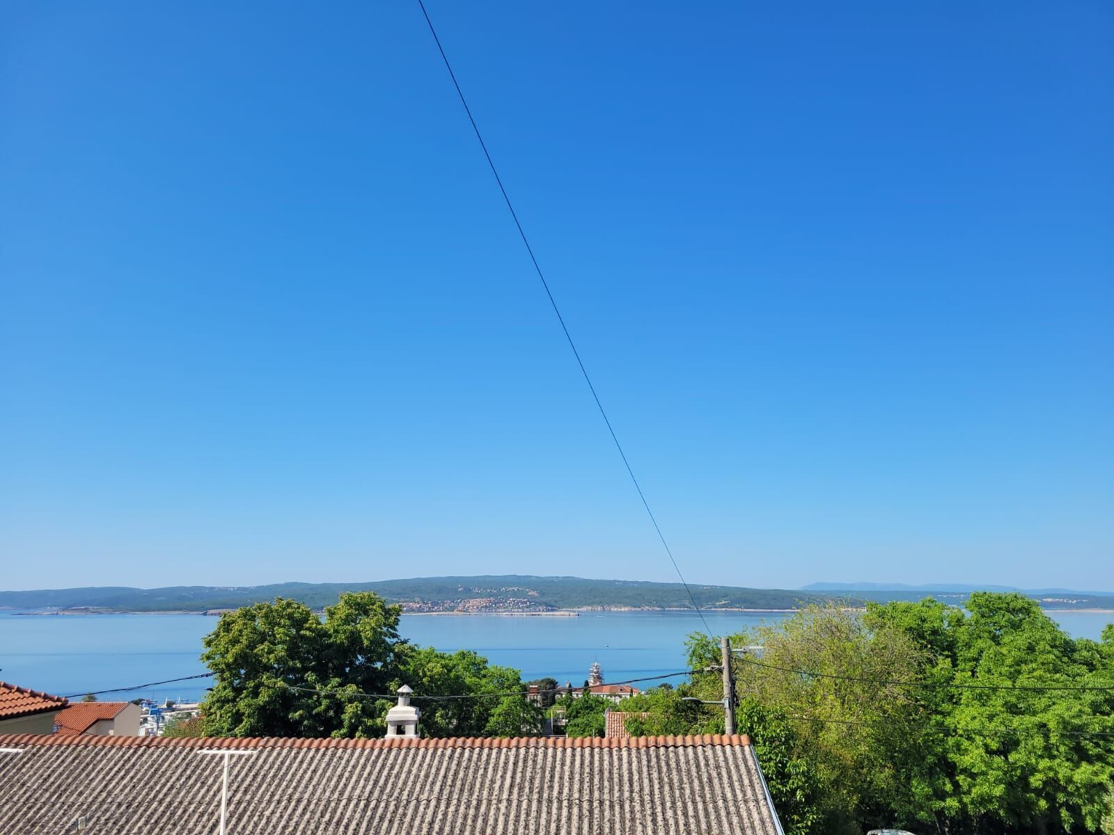 A coastal view with a clear sky, a tiled roof, and a distant town by the sea.