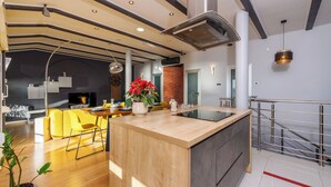 Une cuisine moderne dotée d’un îlot central, d’un coin repas avec des chaises jaunes et d’un escalier avec une rampe en métal.