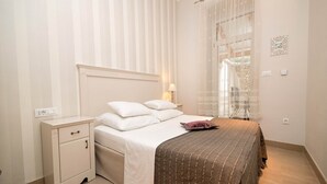 A neatly arranged bedroom with a bed, bedside table, and a window with sheer curtains. - Apartments Latino (Crikvenica)