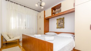 Ένα υπνοδωμάτιο με ένα ξύλινο κρεβάτι, λευκά σεντόνια, μια καρέκλα και μια ντουλάπα.