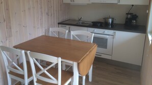 Una cocina compacta con armarios blancos, una mesa de madera y sillas blancas.
