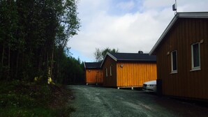 Un camino de grava que lleva a una hilera de cabañas de madera con un bosque de fondo.