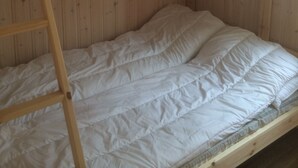 Una cama litera con escalera de madera, ropa de cama blanca y paneles de madera en las paredes.