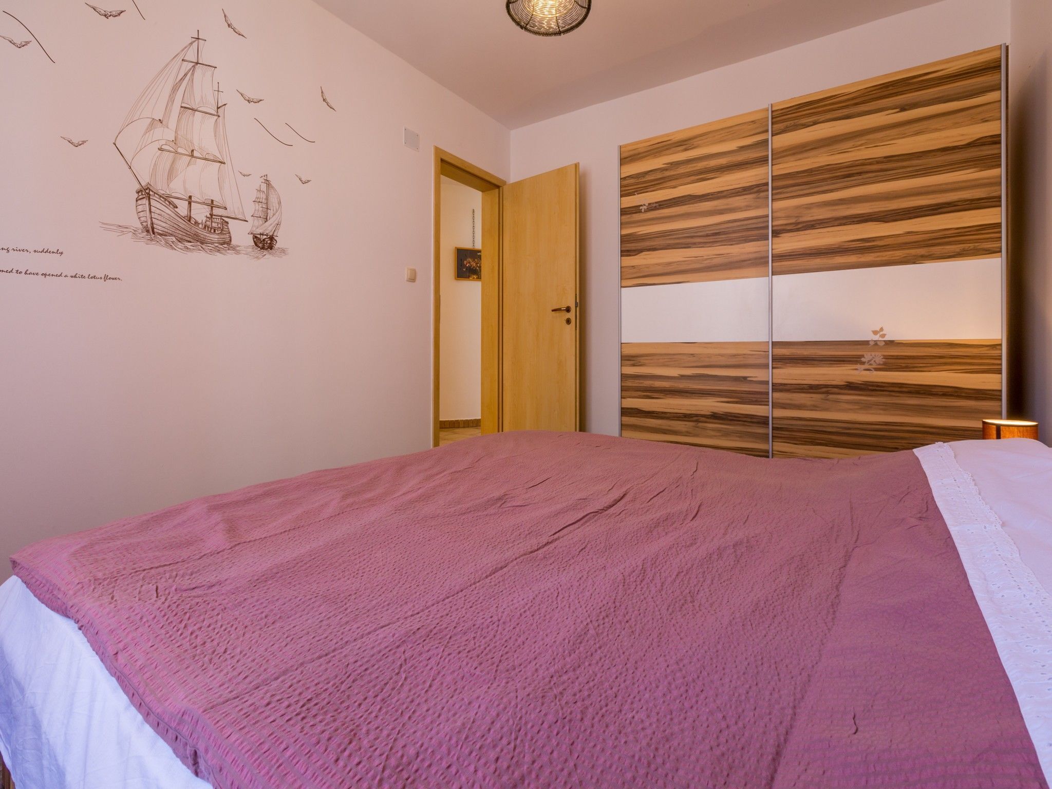 Una camera da letto con un letto grande, un armadio in legno e un affresco raffigurante una nave a vela.