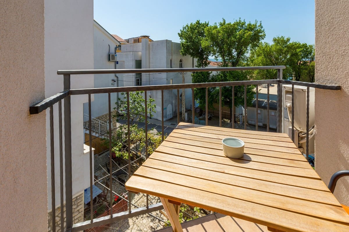 A balcony with a wooden table and a bowl, overlooking a residential area with trees and buildings.