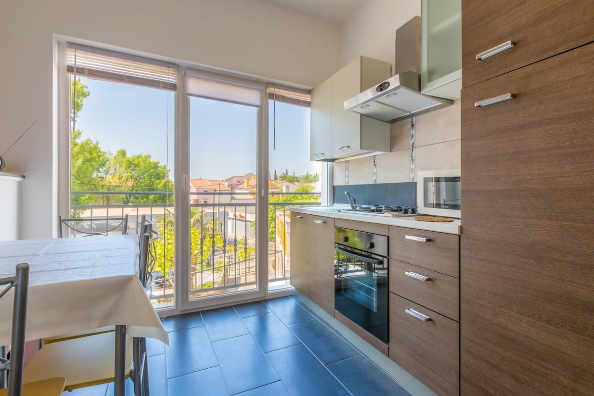 A modern kitchen with a large window, a balcony, and a dining area.