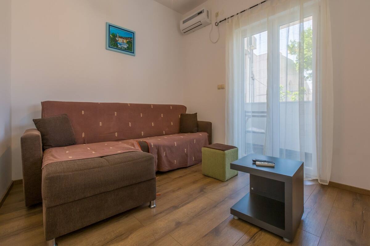 A modern living room with a brown sofa, a small green ottoman, and a grey side table.