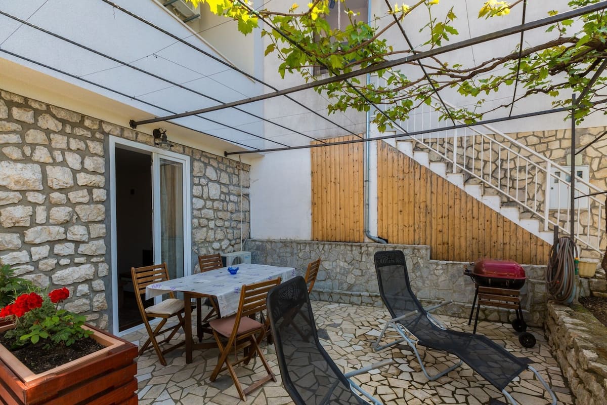 A patio with stone flooring, a table with chairs, a grill, and a staircase.