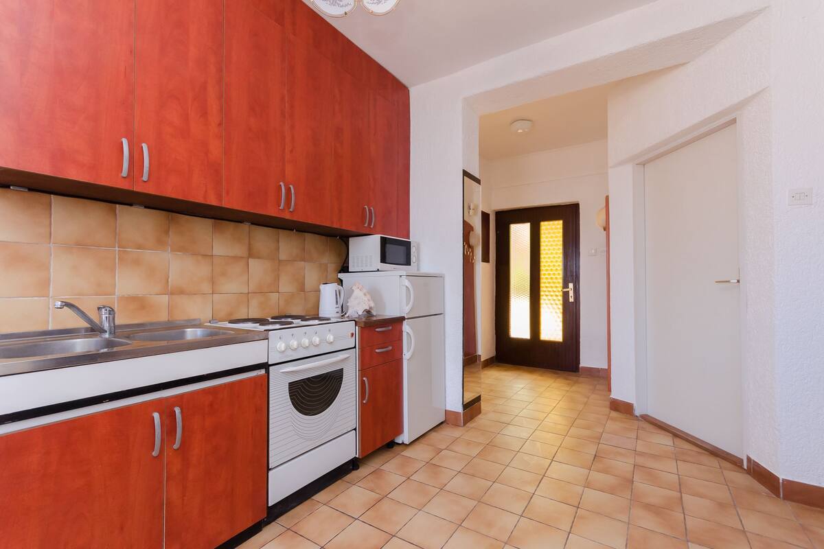 A kitchen with red cabinets, a microwave, a stove, and a sink.