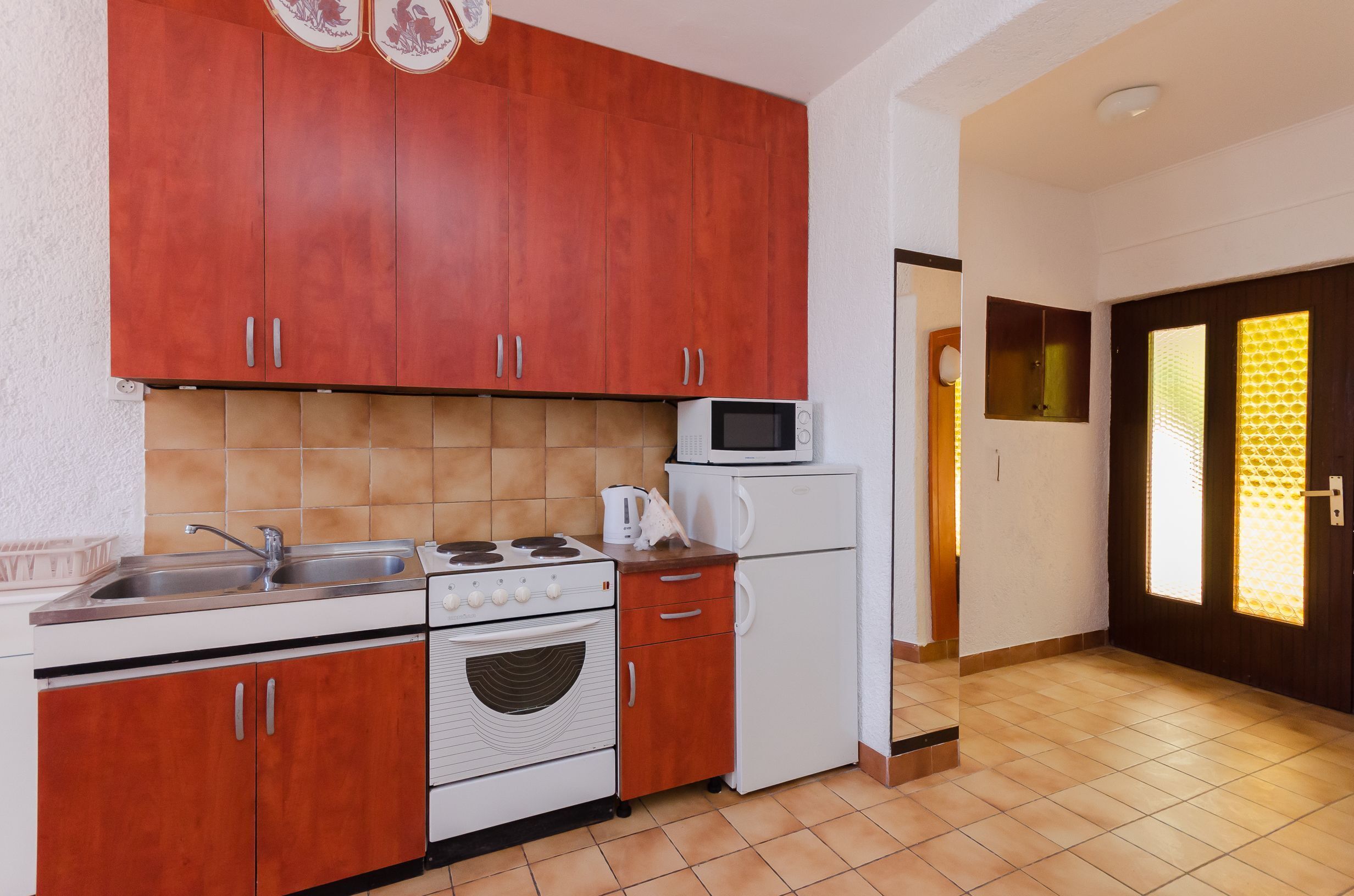 Een kleine keuken met houten kastjes, een magnetron, een fornuis en een koelkast.