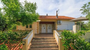 Ein Haus mit Ziegeldach, einer Treppe, die zu einer Tür führt, und einem kleinen Baum im Vordergrund.