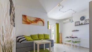 A modern living room with a grey sofa, green cushions, a white coffee table, and a dining area with a white table and chairs. - Apartment Color Green (Dramalj)