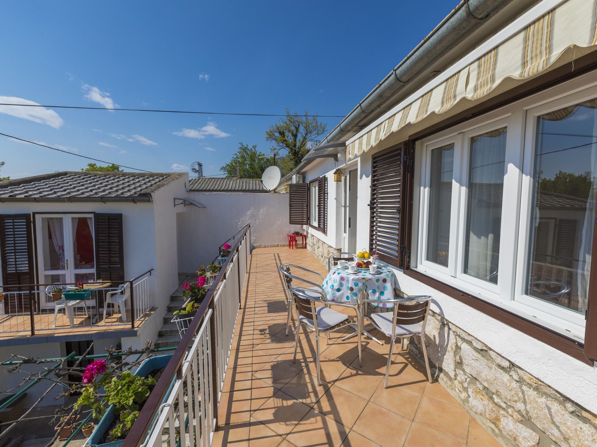 A sunny courtyard with a tiled floor, a table with chairs, and potted plants.