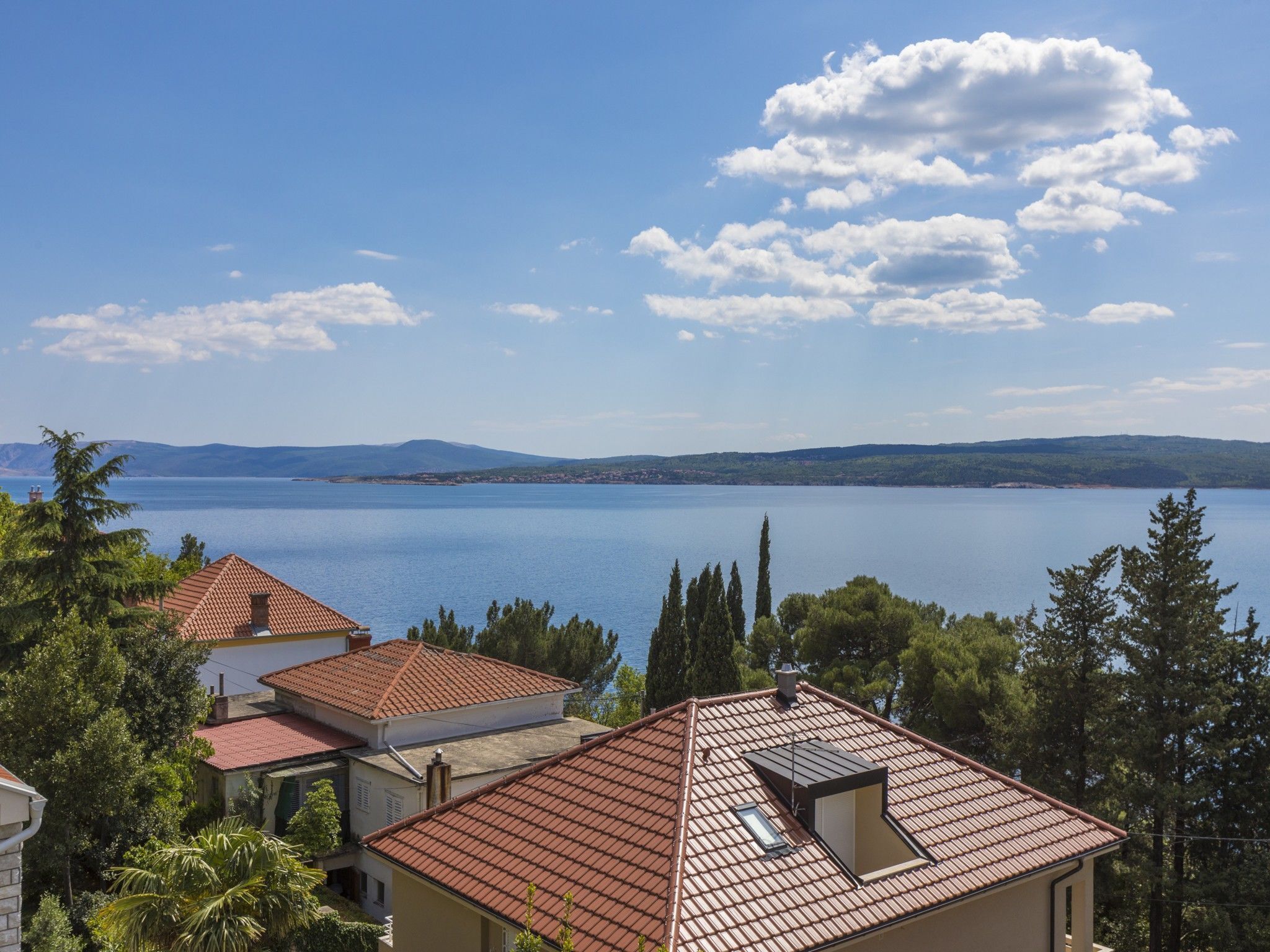 A coastal residential area with houses featuring red-tiled roofs and a large body of water in the background.