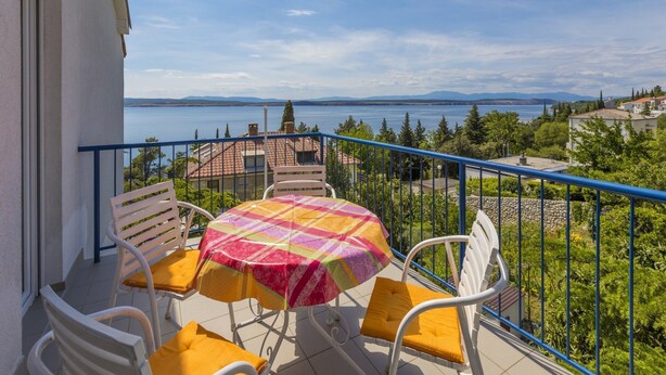 Un balcone con tavolo e sedie, vista su un corpo d'acqua e colline lontane.
